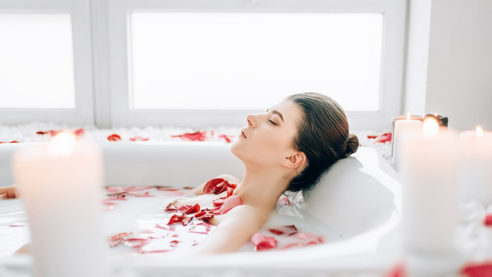 Young woman relaxing in a rose petal bath with scented candles