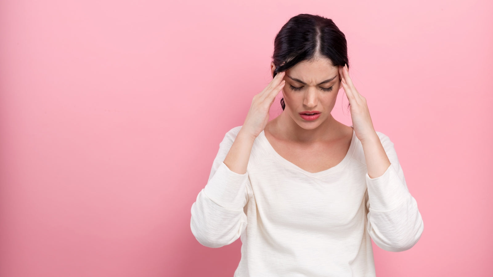 Women in a white sweater touching her head against a pink background